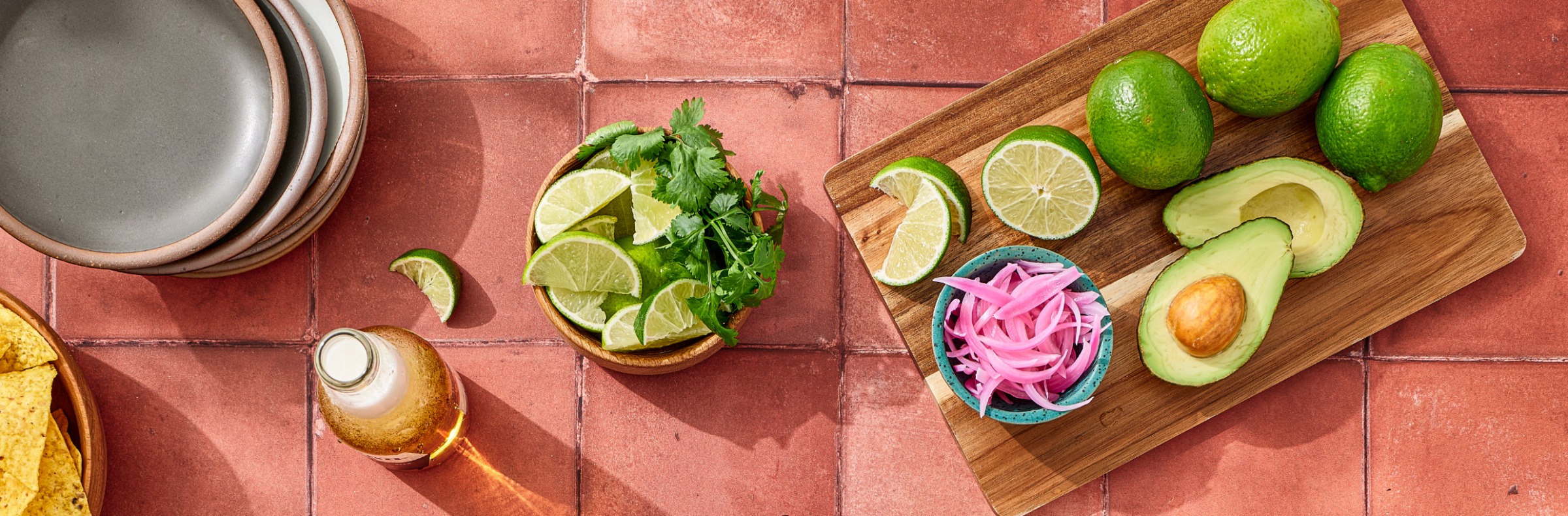 Fresh limes, pickled onions, avocado, and cilantro on a tiled table
